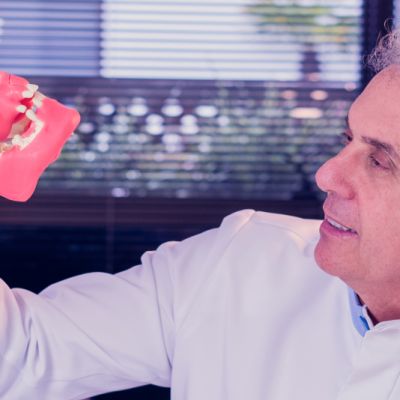Imagem do Dr Paulo com um modelo de crânio na mão, como se estivesse analisando implantes zigomáticos